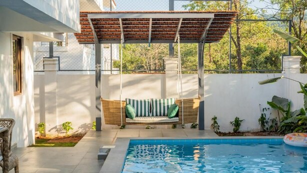 A pool with a swing chair and a pergola, surrounded by a white wall and greenery. - Elivaas Paraíso - Villa Goa (Siolim)