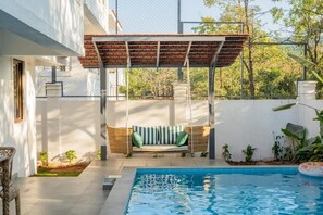 A pool with a swing chair and a pergola, surrounded by a white wall and greenery. - Elivaas Paraíso - Villa Goa (Siolim)
