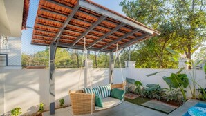 A covered outdoor seating area with a swing chair, a small pool, and a garden with various plants. - Elivaas Paraíso - Villa Goa (Siolim)