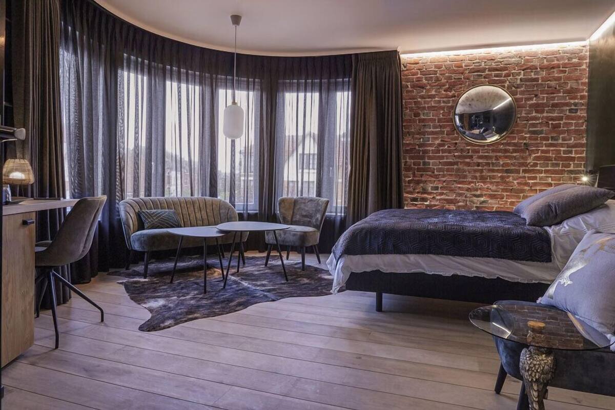 Ein modernes Schlafzimmer mit Backsteinwand, rundem Spiegel, Bett, Schreibtisch und zwei Stühlen.
