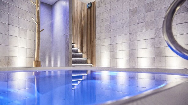 A modern indoor swimming pool with a clear blue water surface, surrounded by grey tiled walls and a wooden panel on one side. - Hôtel Oniro Tournai - Luxury Rooms & Wellnss Suits (Tournai)