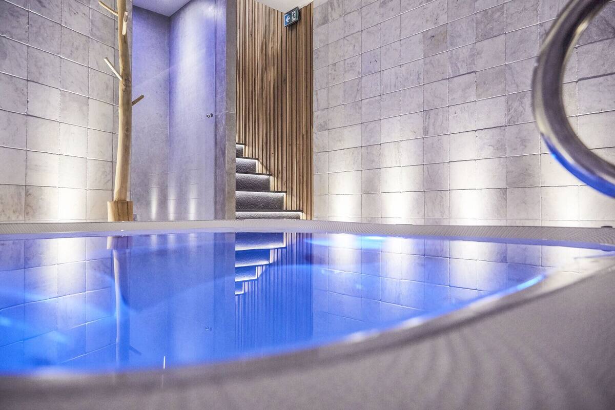Ein modernes Hallenbad mit einer klaren, blauen Wasserfläche, umgeben von grauen Fliesenwänden und einer Holzwand an einer Seite.