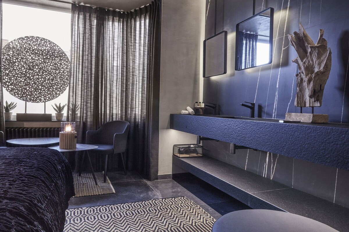 A modern bathroom with a dark blue marble countertop, a round mirror, and a wooden sculpture.