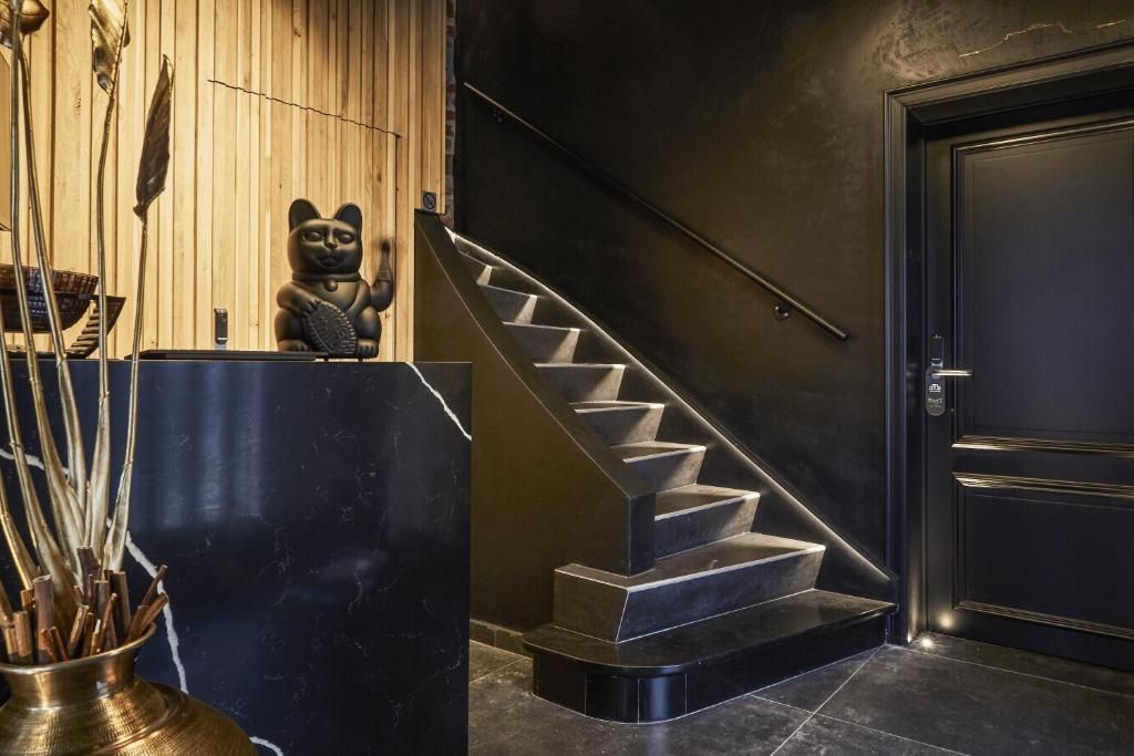 Um interior moderno com uma escada preta, uma mesa de recepção e uma estátua decorativa de gato.