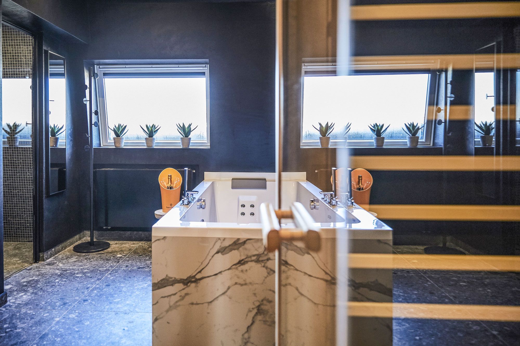 Een moderne kamer met een tafelvoetbaltafel, grote ramen met plantenbakken en een marmeren vloer.