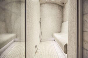 A small, tiled shower stall with a glass door, a showerhead, and a bench.