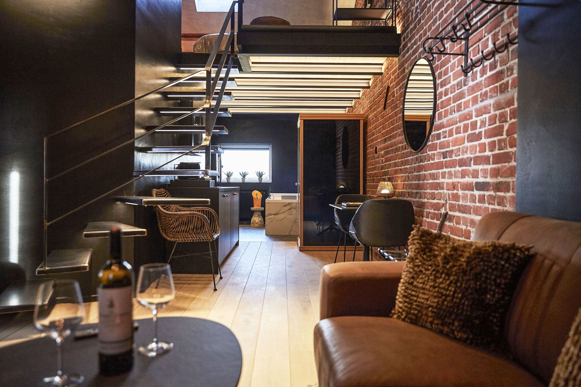 A modern interior with a staircase, a dining area with a table and chairs, and a brick wall.