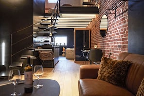 A modern interior with a staircase, a dining area with a table and chairs, and a brick wall. - Hôtel Oniro Tournai - Luxury Rooms & Wellnss Suits (Tournai)