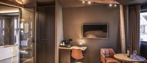 Un dormitorio moderno con ducha de vidrio, techo de madera, una mesa redonda con una copa de vino y una cama grande.