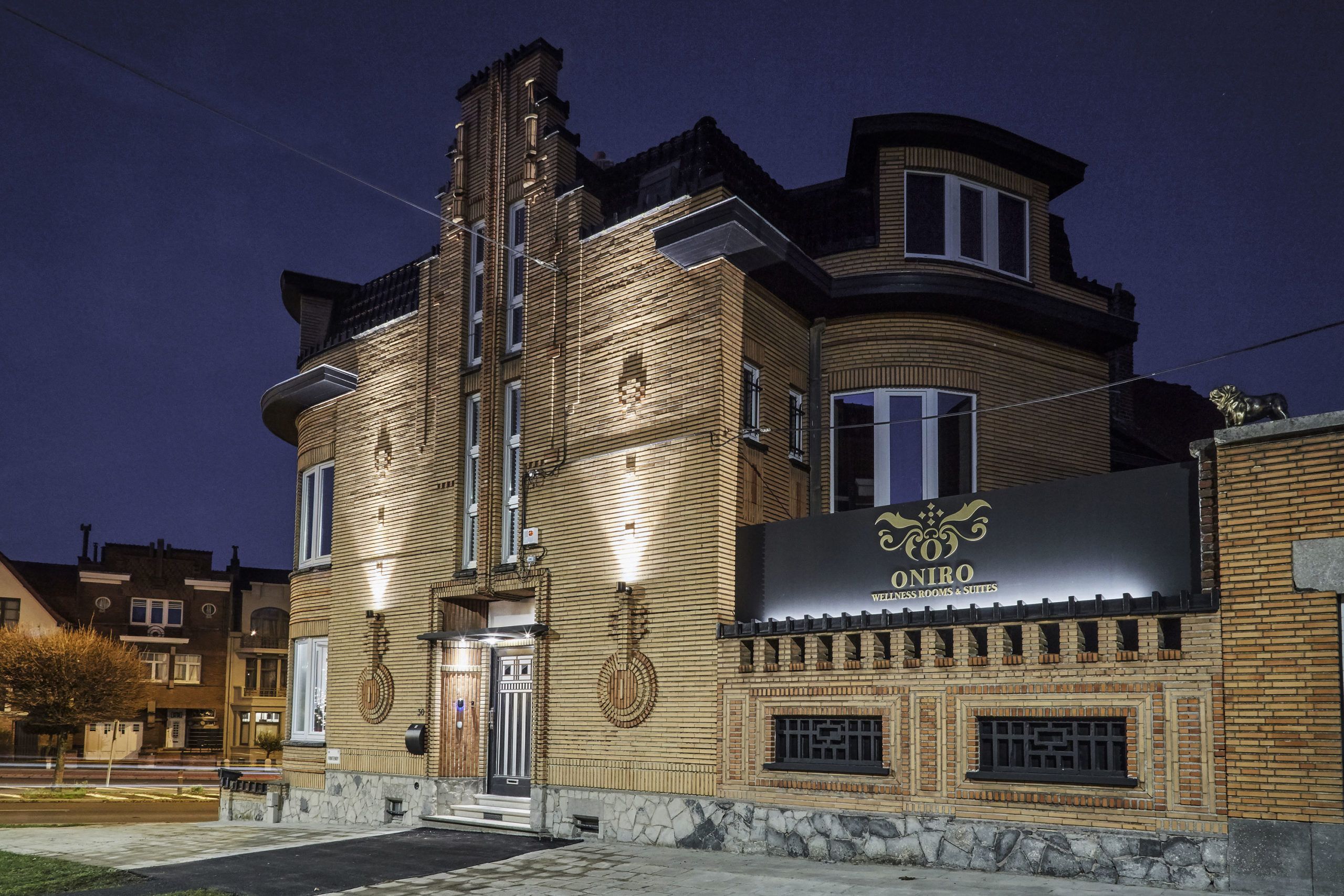 Rakennus, jonka yläpuolella on yöllä valaistu kyltti, jossa lukee: ”ONIRO WELLNESS ROOMS & SUITES”.