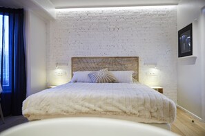 A bedroom with a white brick wall, a wooden headboard, two bedside lamps, and a bed with a white duvet. - Hôtel Oniro Tournai - Luxury Rooms & Wellnss Suits (Tournai)