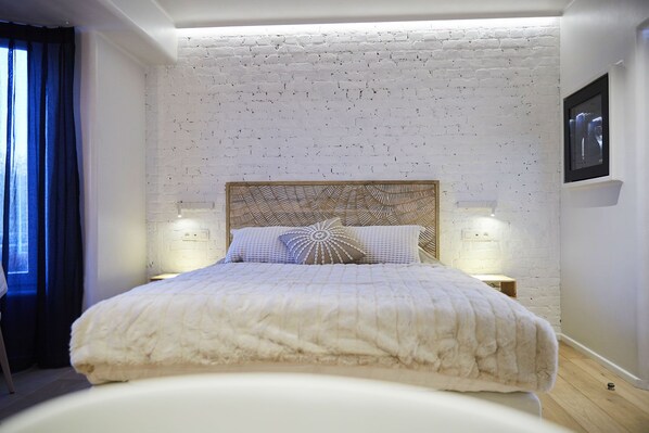 A bedroom with a white brick wall, a wooden headboard, two bedside lamps, and a bed with a white duvet. - Hôtel Oniro Tournai - Luxury Rooms & Wellnss Suits (Tournai)