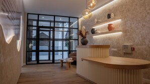 Een moderne receptie met een houten balie, een glazen deur en een wandplank met decoratieve objecten.