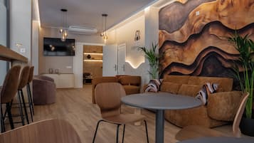 A modern interior with a wooden floor, a round table, and a sofa. There is a TV mounted on the wall and a plant in the corner.
