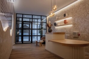 Een moderne receptie met een houten balie, een glazen deur en een wandplank met decoratieve objecten.