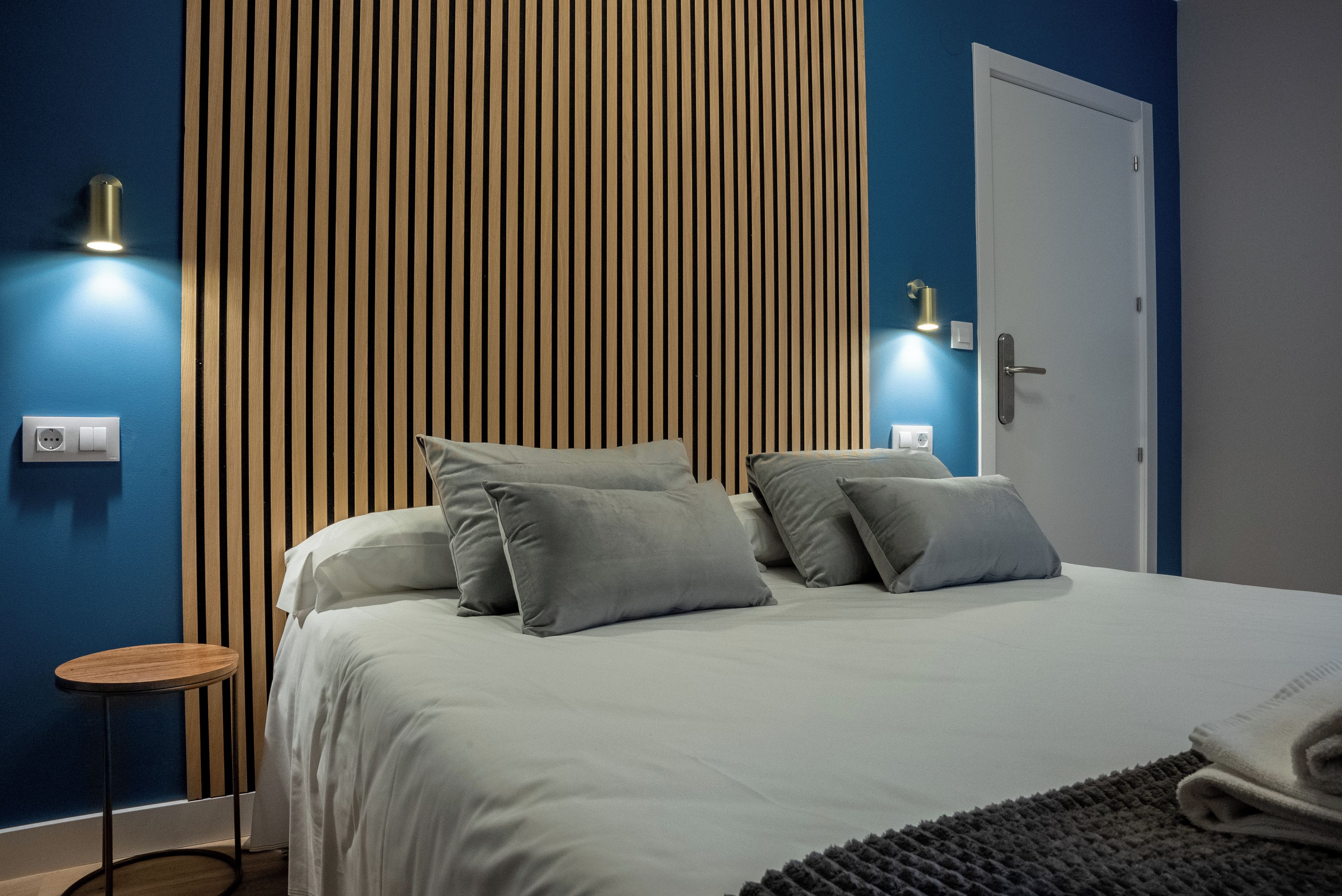 A modern bedroom with a bed, pillows, a bedside table, and a wall-mounted light fixture.