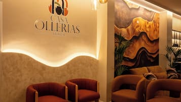 A hotel lobby with a modern design, featuring a logo on the wall, a seating area with chairs, and a decorative wall mural.