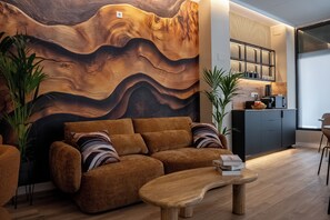 Een moderne woonkamer met een grote wand van hout in een golvend patroon, een bruine bank, een houten salontafel en een keuken met een inbouwboekenplank.