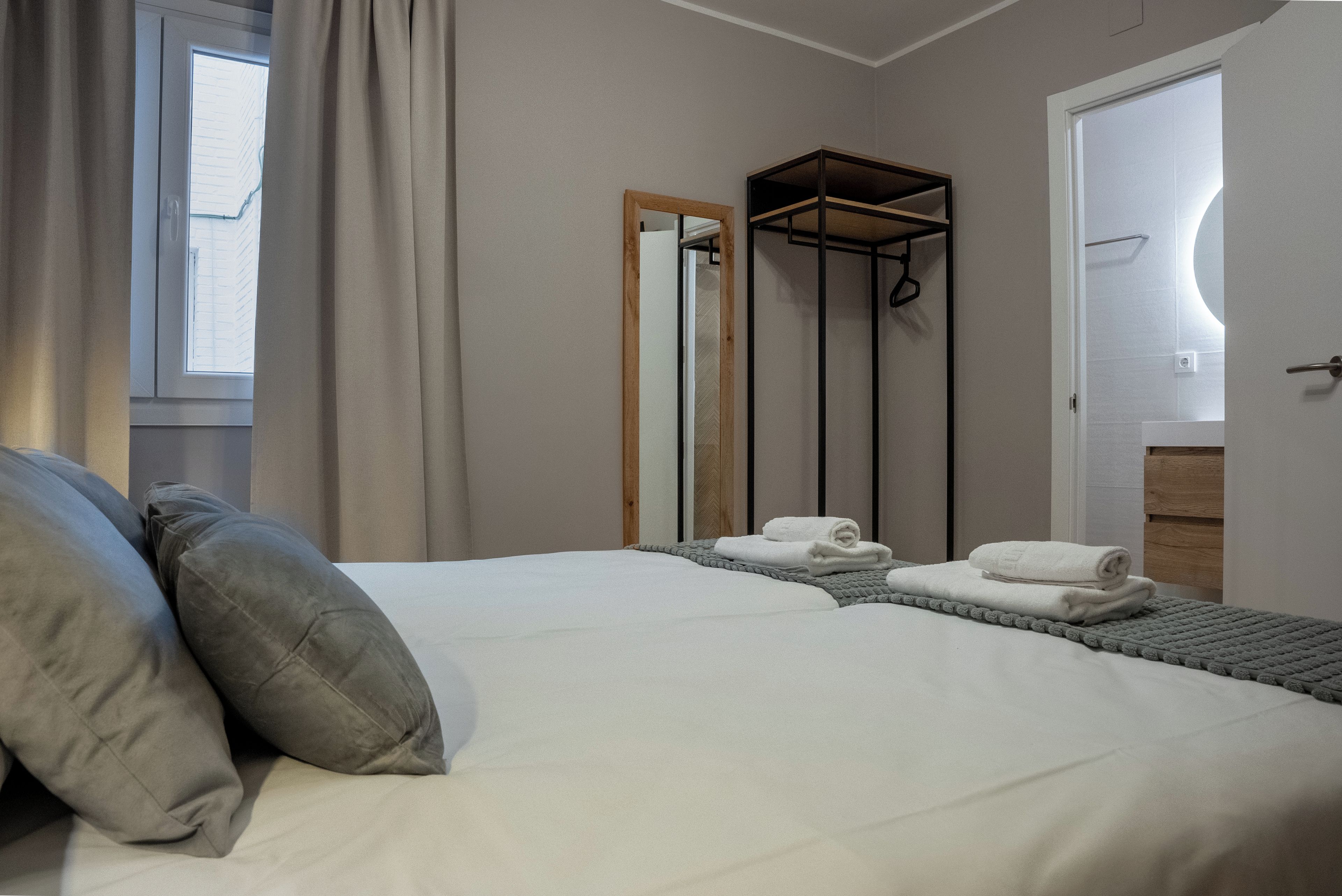 Un lit bien fait, avec des oreillers, un porte-serviettes et un miroir, dans une chambre d’hôtel.