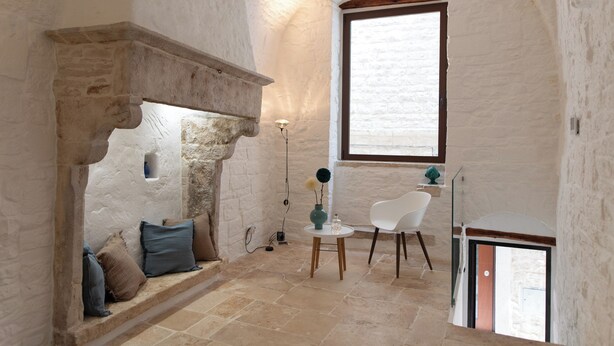 A room with a stone fireplace, a white chair, and a small table with a vase. - Ad Calcem "lagodentro" (Terlizzi)