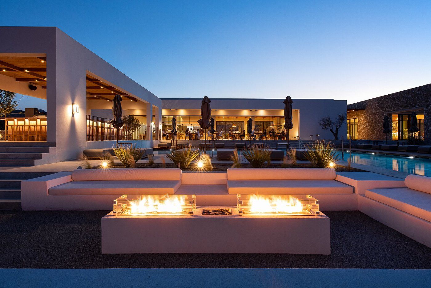 Un área de piscina moderna al aire libre con asientos integrados y una chimenea.