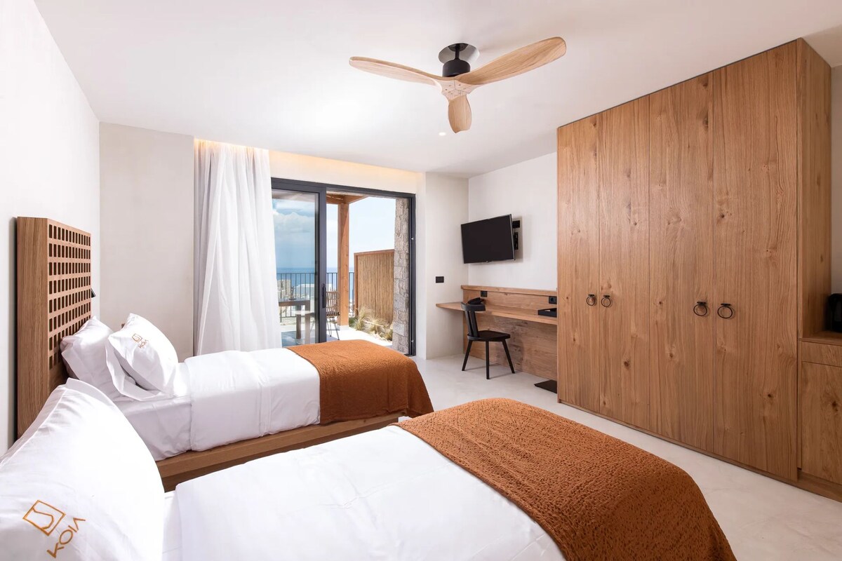 A hotel room with two beds, a desk, a TV, and a balcony with a view.