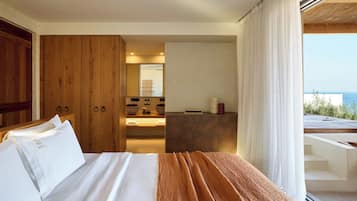 Une chambre avec un lit, une armoire en bois, une salle de bain avec un lavabo et un miroir, et un balcon avec vue sur la mer.