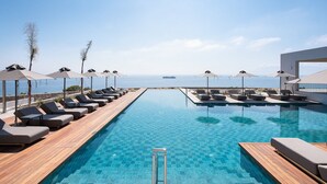 A poolside area with lounge chairs and umbrellas, a wooden deck, and a view of the sea. - Koia All-suite Wellbeing Resort (Kos)