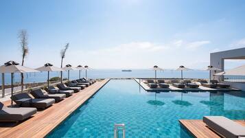 Un área junto a la piscina con sillones de descanso y sombrillas, una terraza de madera y vista al mar.