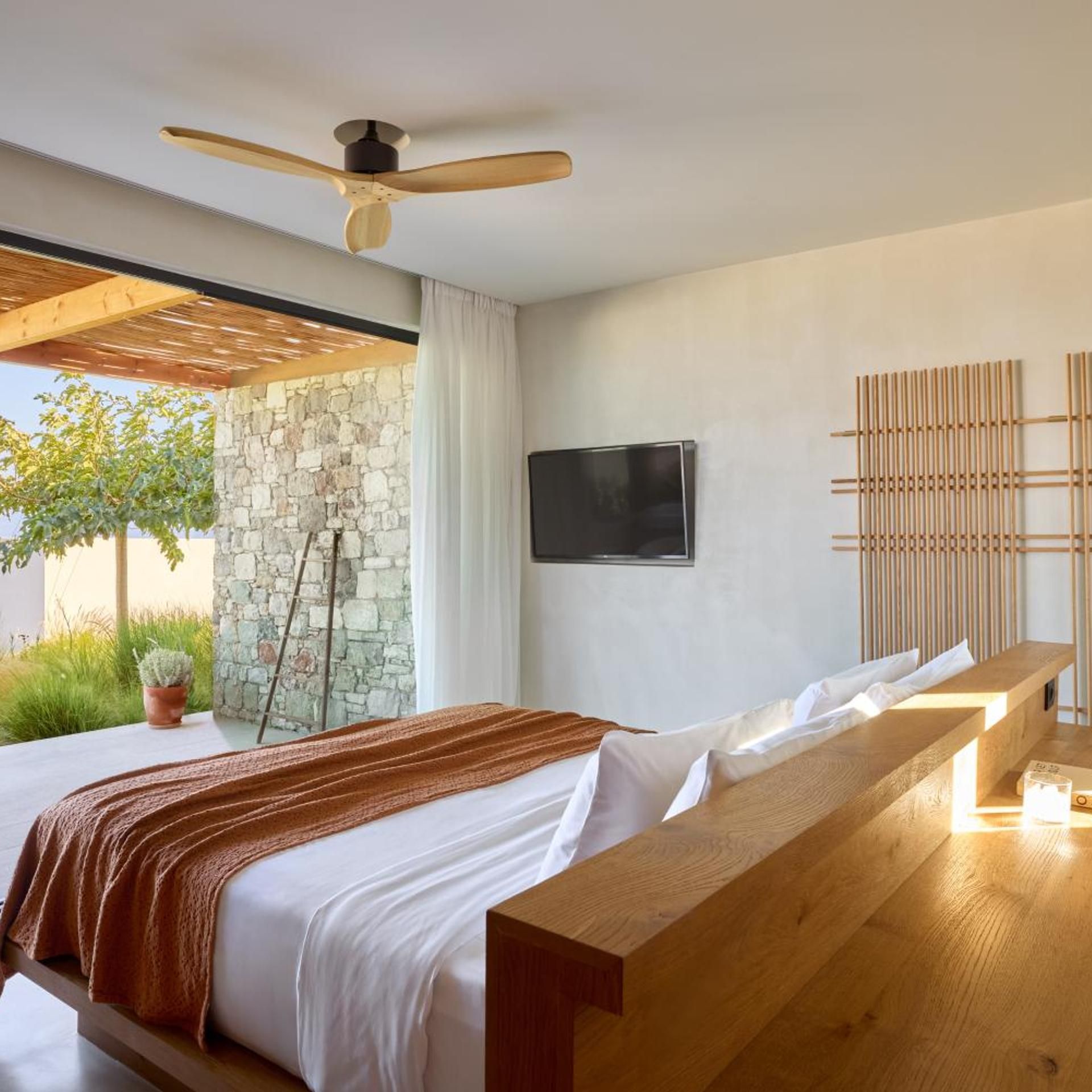 A modern bedroom with a bed, a bench, a TV, and a stone wall.