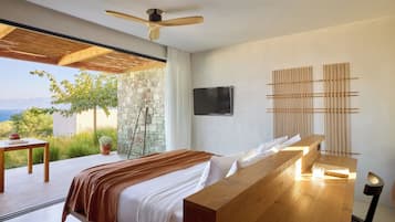A modern bedroom with a large bed, wooden headboard, a ceiling fan, a stone wall, a TV, and a view of the outdoors.