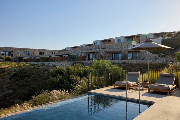 A modern villa with a pool, outdoor seating, and a stone facade. - Koia All-suite Wellbeing Resort (Kos)