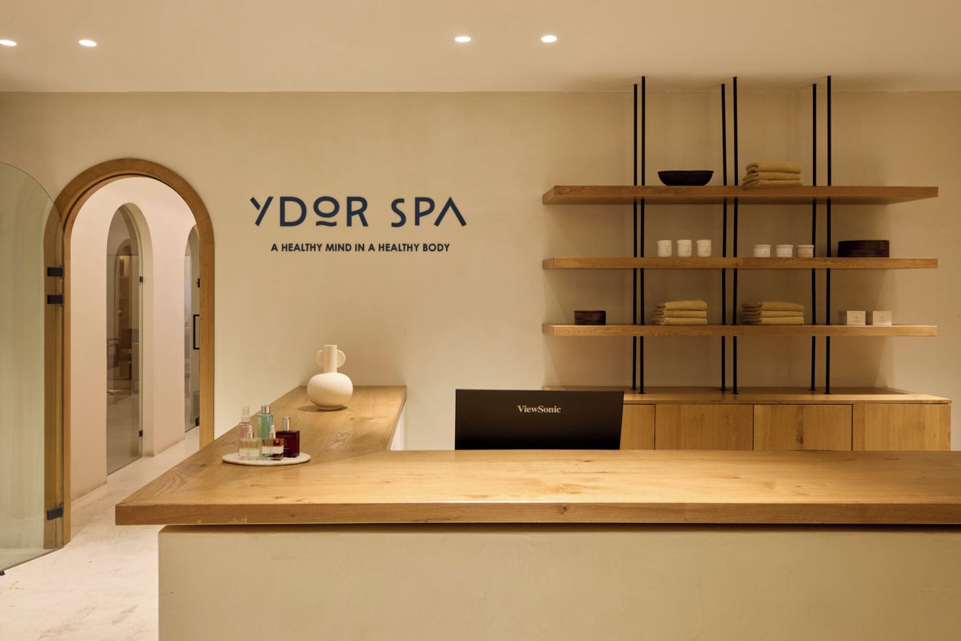 Un espace d’accueil avec un comptoir en bois, une enseigne indiquant « YDR SPA : un esprit sain dans un corps sain » et un écran ViewSonic.