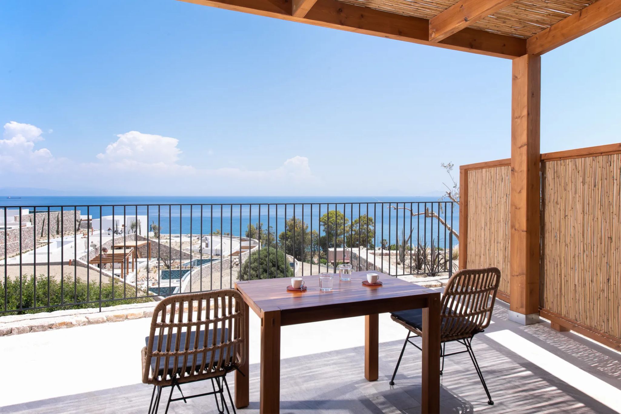 A wooden table with two chairs on a balcony overlooking a beach and the sea.