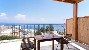A wooden table with two chairs on a balcony overlooking a beach and the sea.