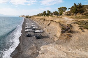 A beach with sun loungers and umbrellas, a rocky shoreline, and sparse vegetation.