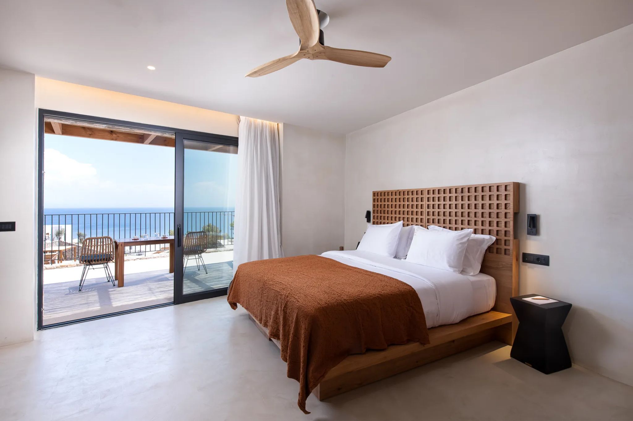 Ein Schlafzimmer mit Bett, Deckenventilator, Meerblick und einem Balkon mit Gartenmöbeln.