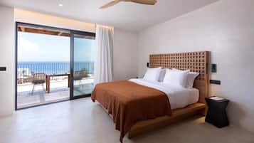 Ein Schlafzimmer mit Bett, Deckenventilator, Meerblick und einem Balkon mit Gartenmöbeln.