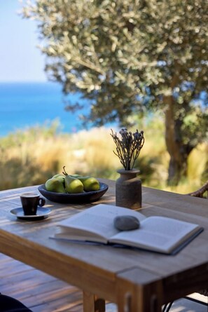 A wooden table with a bowl of green apples, a cup, a book, and a stone. - Koia All Suite Wellbeing Resort (Kos)
