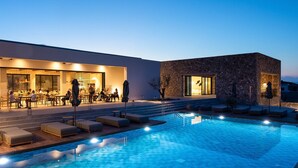 A swimming pool with lounge chairs and a restaurant area. - Koia All-suite Wellbeing Resort (Kos)
