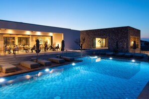 A swimming pool with lounge chairs and a restaurant area. - Koia All-suite Wellbeing Resort (Kos)