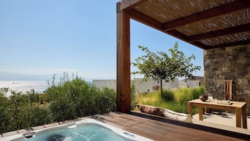 A hot tub with a wooden deck, a stone wall, and a view of the sea.
