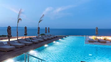 Ein Poolbereich mit Liegestühlen und Sonnenschirmen, mit Blick auf das klare Meer und einem gefliesten Pool.