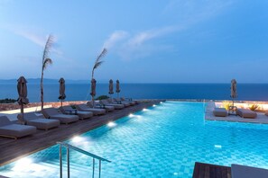 A poolside area with lounge chairs and umbrellas, a clear view of the sea, and a tiled pool. - Koia All-suite Wellbeing Resort (Kos)