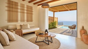 A modern living room with a sofa, coffee table, and a view of the ocean through a sliding glass door. - Koia All-suite Wellbeing Resort (Kos)