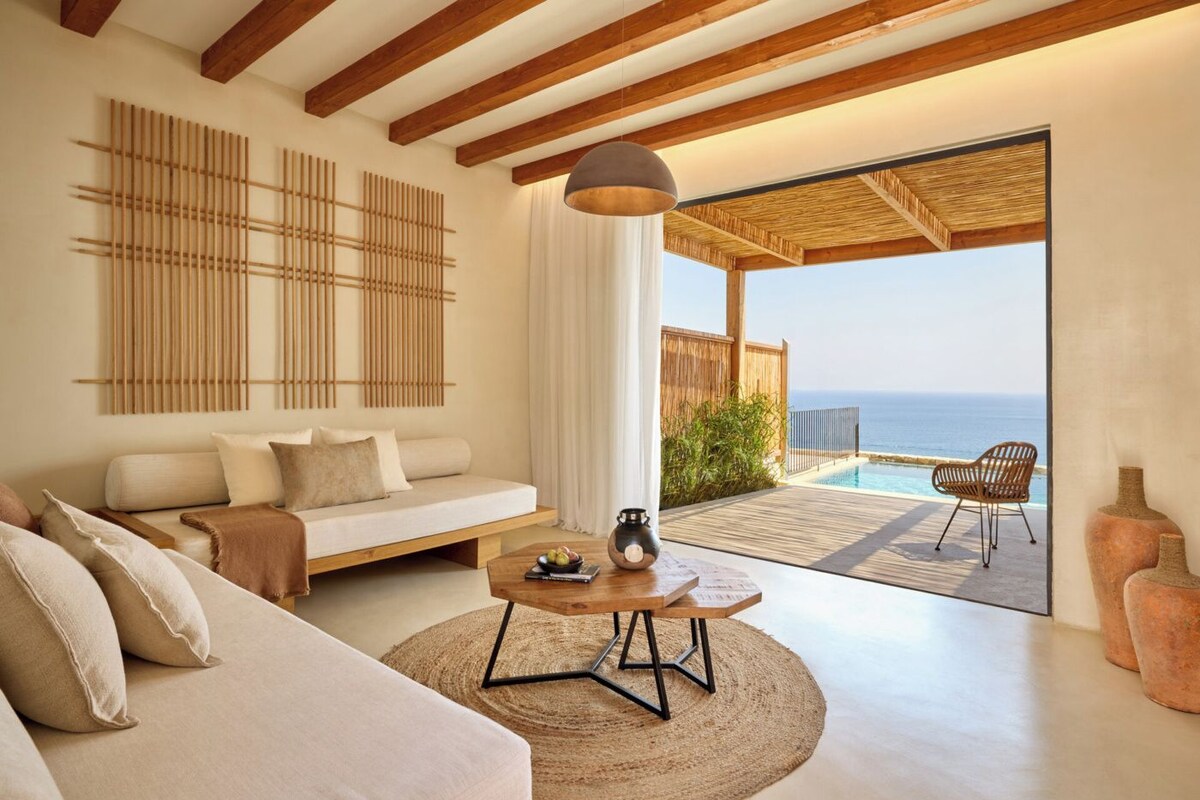 A modern living room with a sofa, coffee table, and a view of the ocean through a sliding glass door.