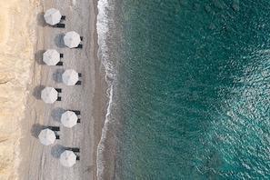 An aerial view of a beach with umbrellas and lounge chairs arranged along the shoreline. - Koia All-suite Wellbeing Resort (Kos)