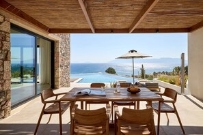 An outdoor dining area with a view of the sea, a pool, and a mountain range. - Koia All-suite Wellbeing Resort (Kos)