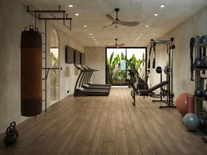 A gym with wooden flooring, exercise equipment, a punching bag, and a view of greenery through large windows. - Koia All Suite Wellbeing Resort (Kos)