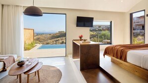 A modern hotel room with a large bed, a desk, a TV, and a view of a mountainous landscape. - Koia All-suite Wellbeing Resort (Kos)